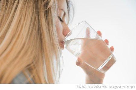Eine Frau trinkt aus einem Glas klarem Leitungswasser. Ein Wassertest auf Blei hilft Ihnen, den Schadstoff zu erkennen.